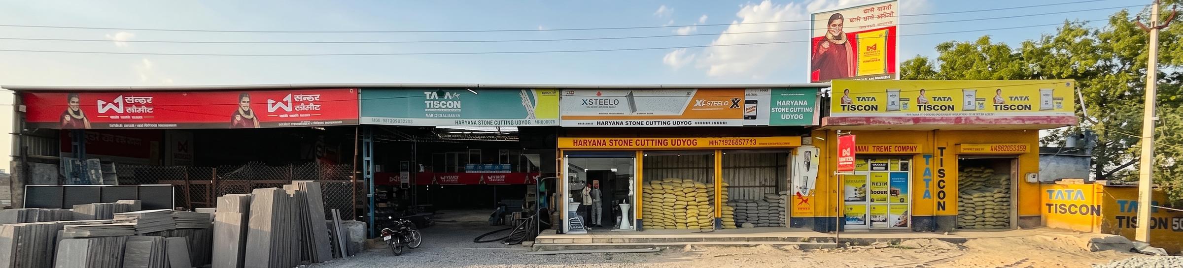 Haryana Trading Company and Haryana Stone Cutting Udyog shopfront on Behror Road, with stacked stone slabs, cement stock and TMT steel signage